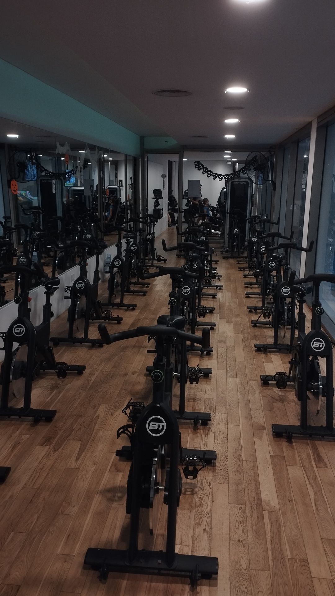 Indoor cycling studio with rows of stationary bikes on wooden flooring and Halloween decorations.