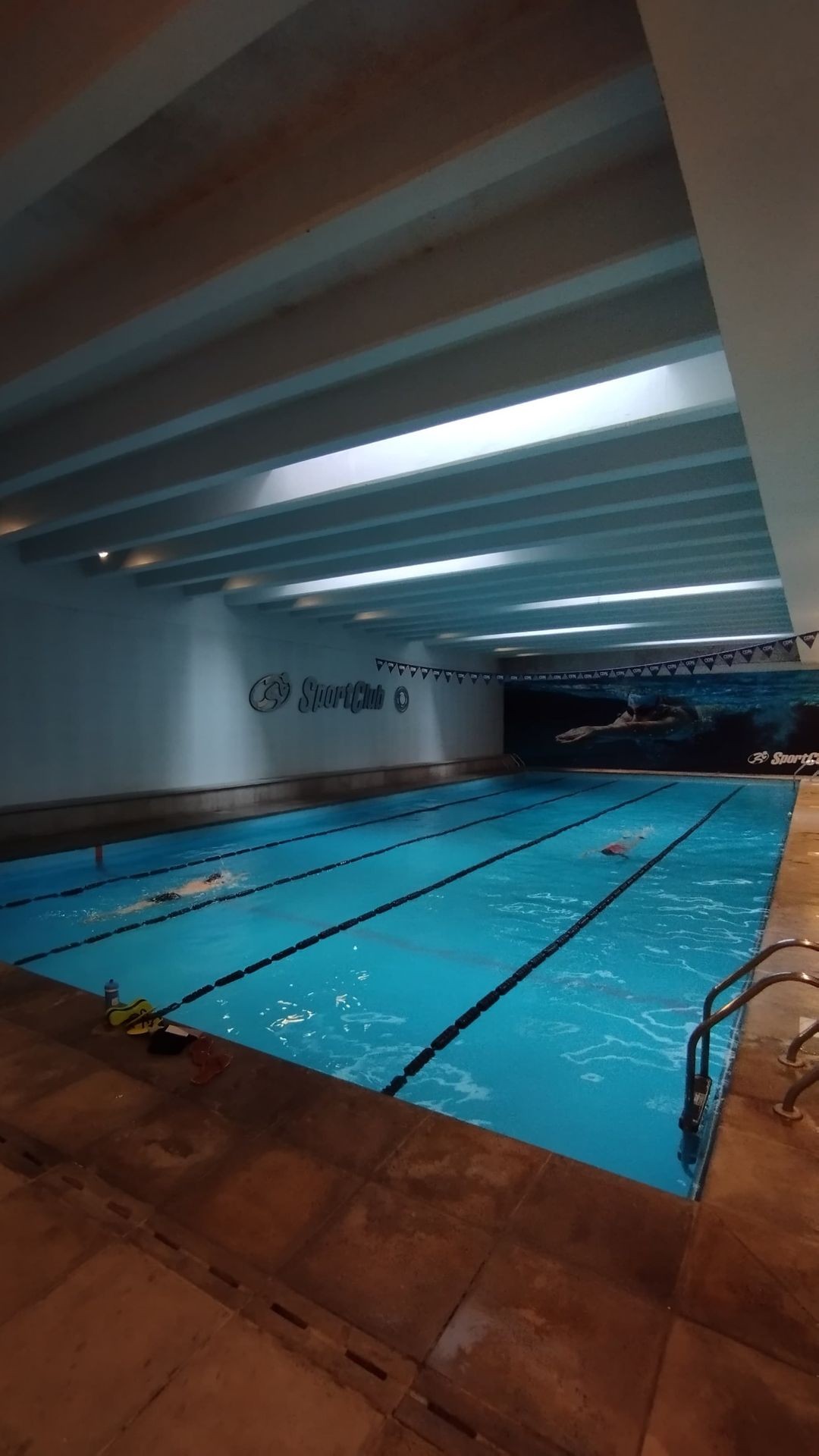 Indoor swimming pool with lanes, swimmer practicing, and a SportClub logo on the wall.