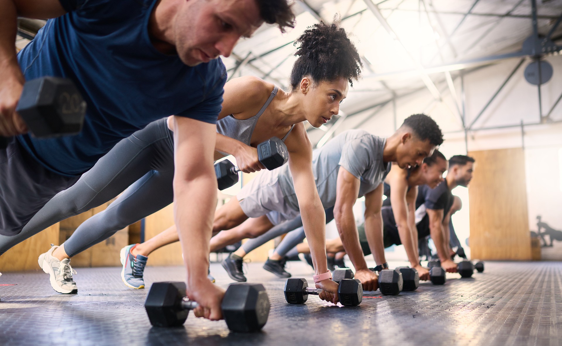 Personas fuertes, fitness y gimnasio con entrenamiento de trabajo en equipo con mancuernas o ejercicio comunitario, responsabilidad y grupo. Amigos de la diversidad deportiva en el piso en entrenamiento muscular pushup, potencia y bienestar juntos