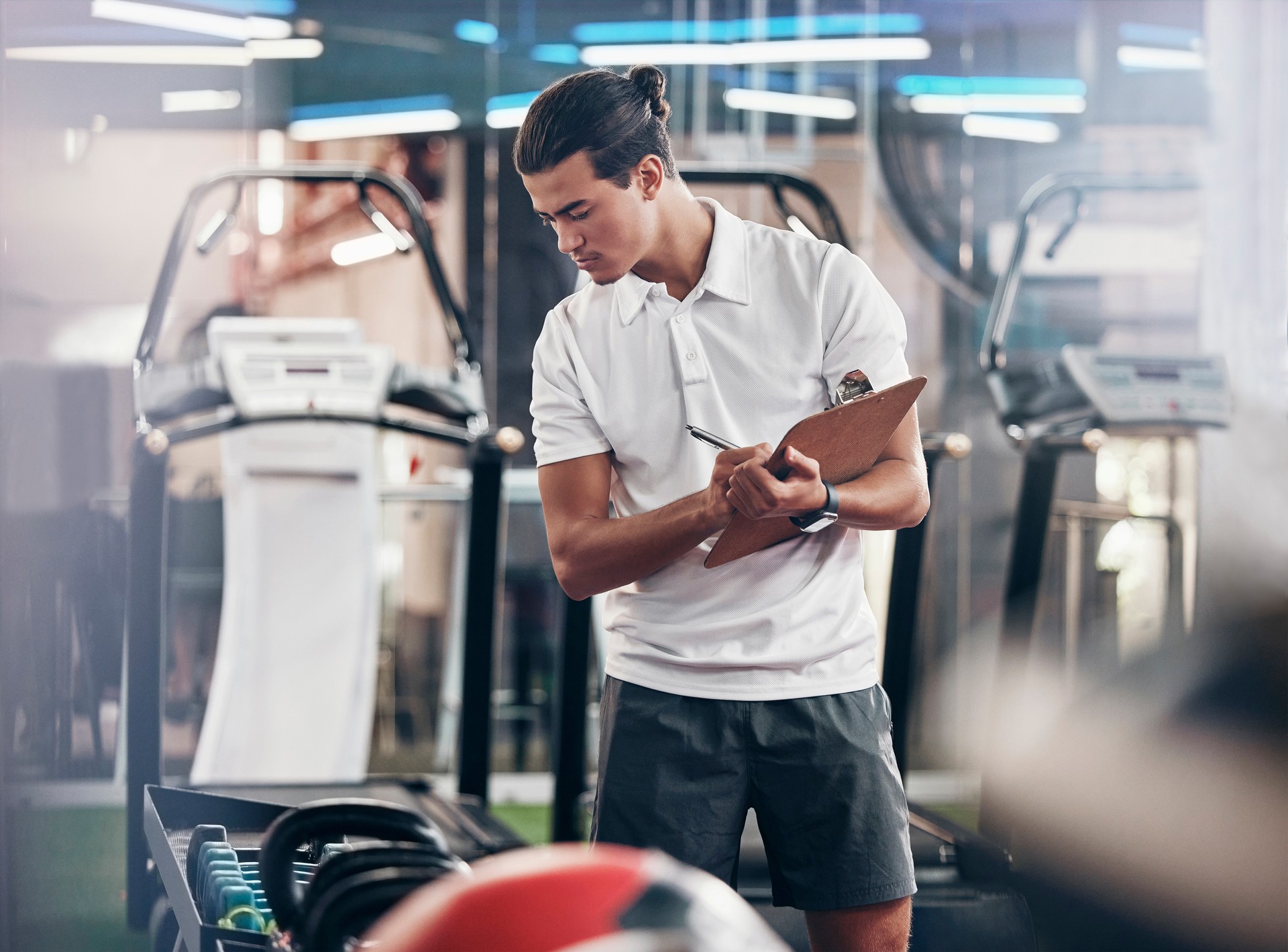 Gimnasio, entrenador y portapapeles con un gerente de hombre revisando el equipo en el gimnasio y escribiendo notas. Líder, entrenador personal y hombre atlético revisando pesas de ejercicio en un club de salud para prepararse